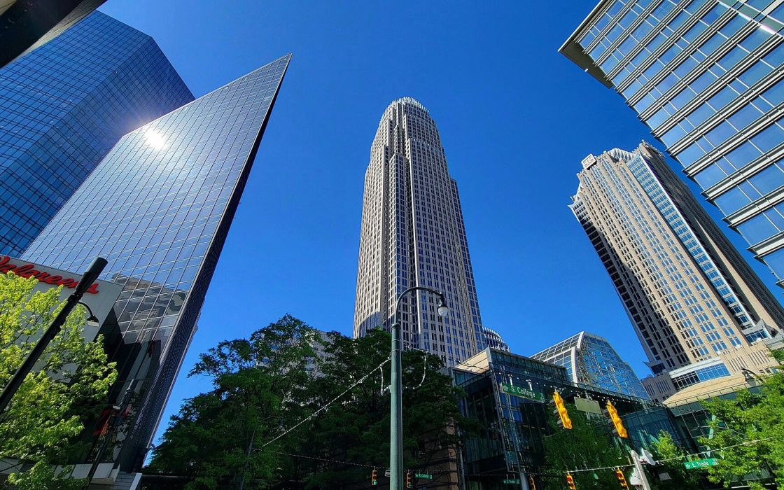 Low-angle view of the Bank of America Corporate Center skyscraper surrounded by glass office towers under a blue sky