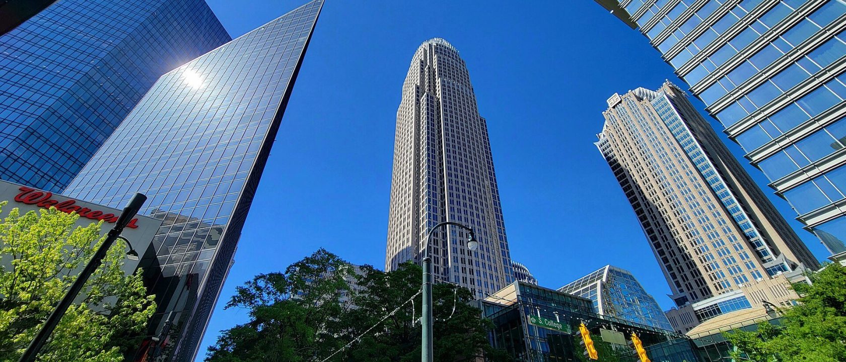 Low-angle view of the Bank of America Corporate Center skyscraper surrounded by glass office towers under a blue sky