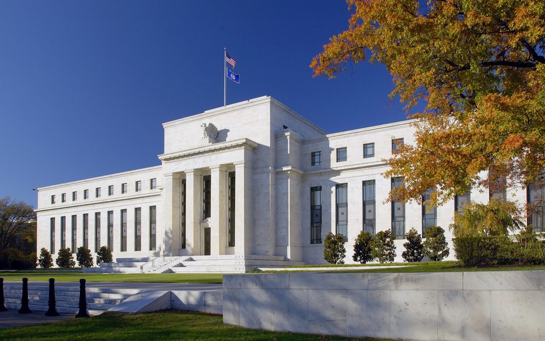 White marble Eccles Building of the Federal Reserve under a blue sky with orange autumn trees