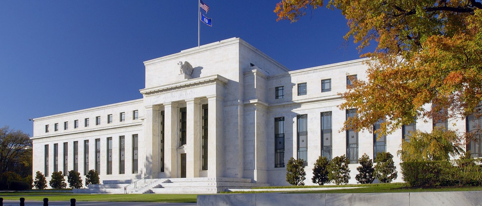 White marble Eccles Building of the Federal Reserve under a blue sky with orange autumn trees