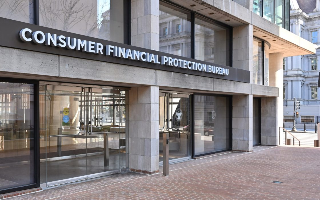 Glass entrance of the CFPB headquarters building with the bureau's name in raised letters above the doors