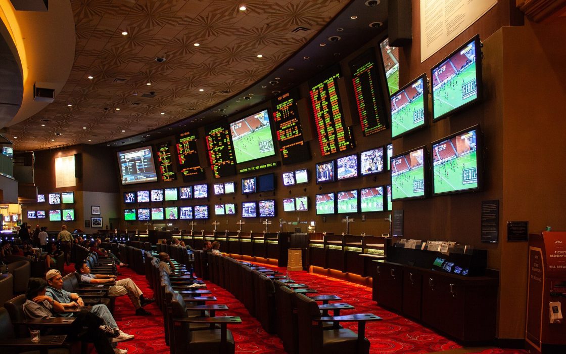 Casino sportsbook with wall of TV screens and odds boards above rows of seats