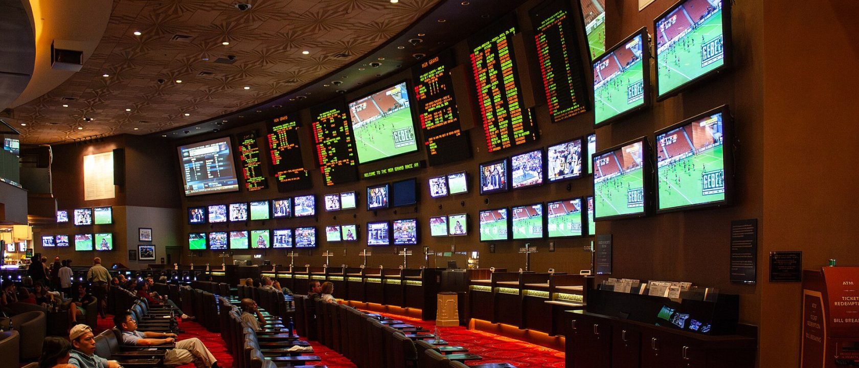 Casino sportsbook with wall of TV screens and odds boards above rows of seats