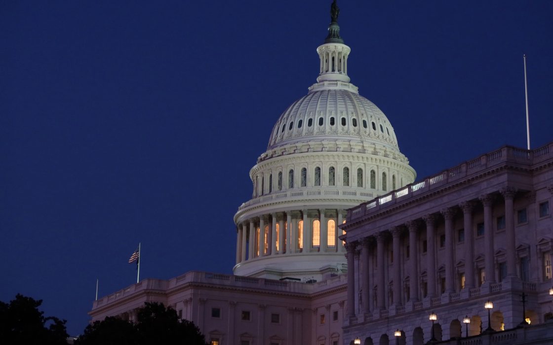 The illuminated dome of the United States Capitol against a dark blue evening sky