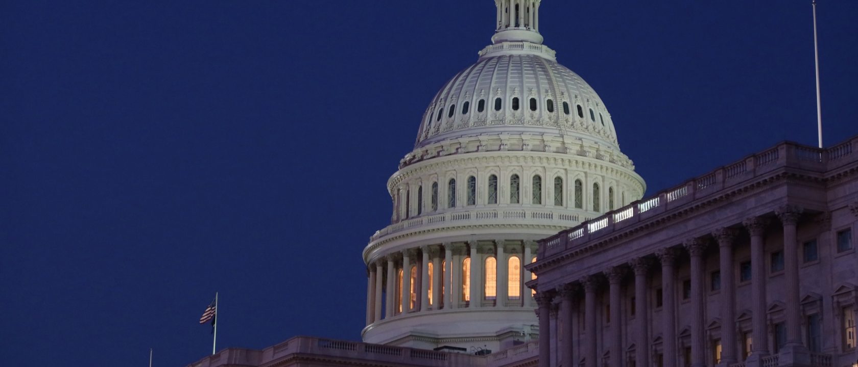 The illuminated dome of the United States Capitol against a dark blue evening sky