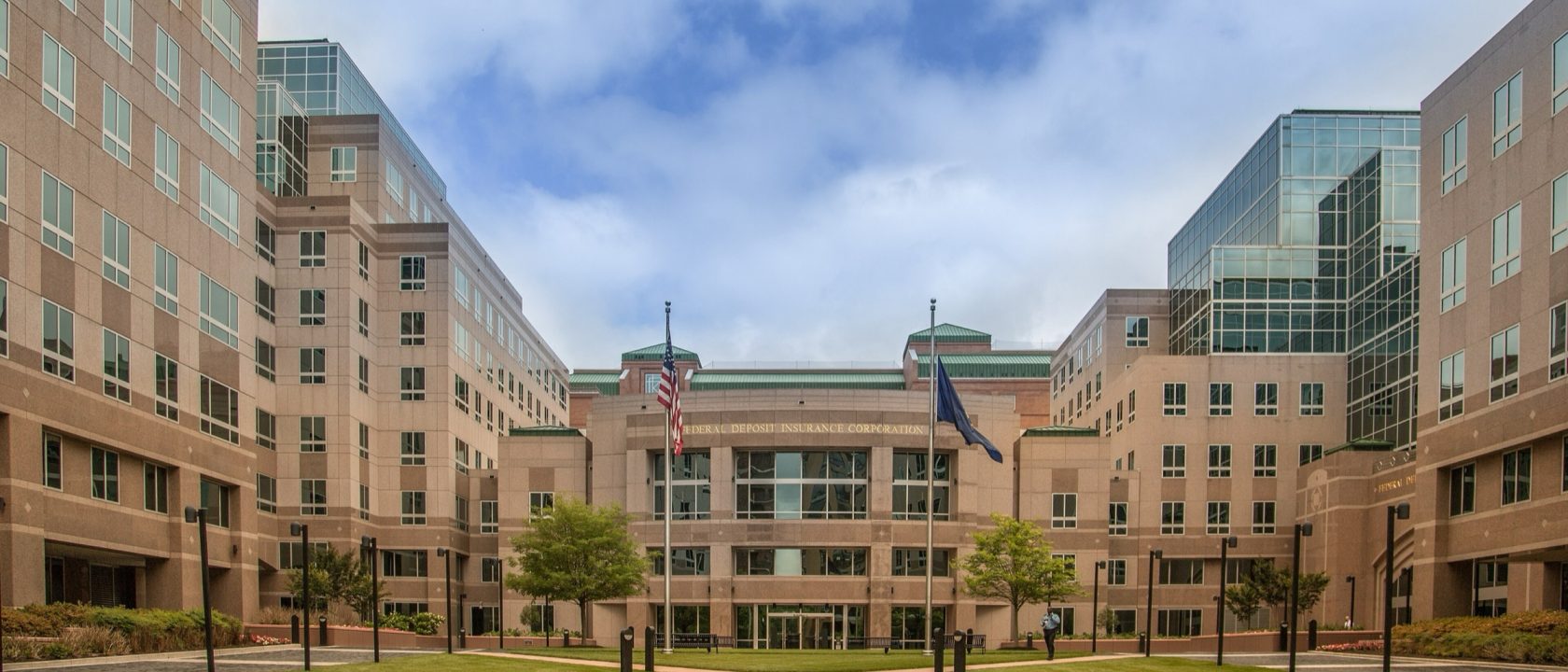 Tan brick office buildings around a lawn with benches and two flagpoles at the FDIC campus in Arlington, Virginia
