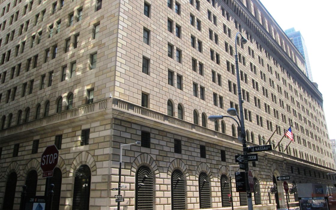 Stone facade of the Federal Reserve Bank of New York building on a Lower Manhattan street corner