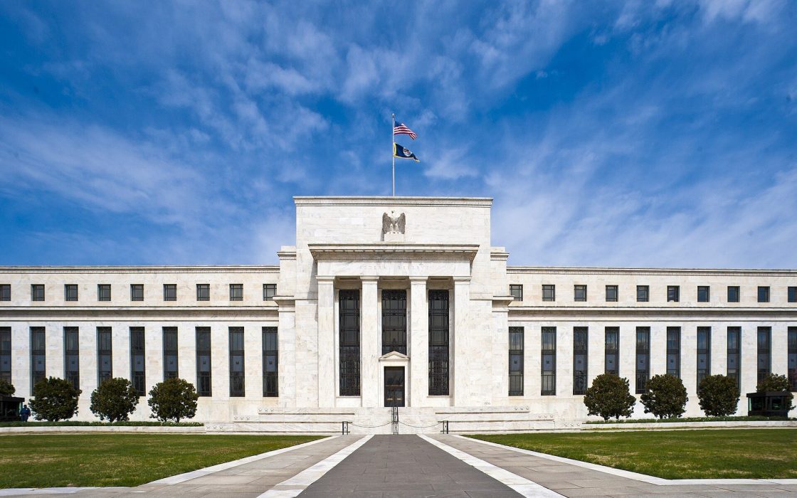 Front facade of the white marble Eccles Building with an American flag on top under a blue sky