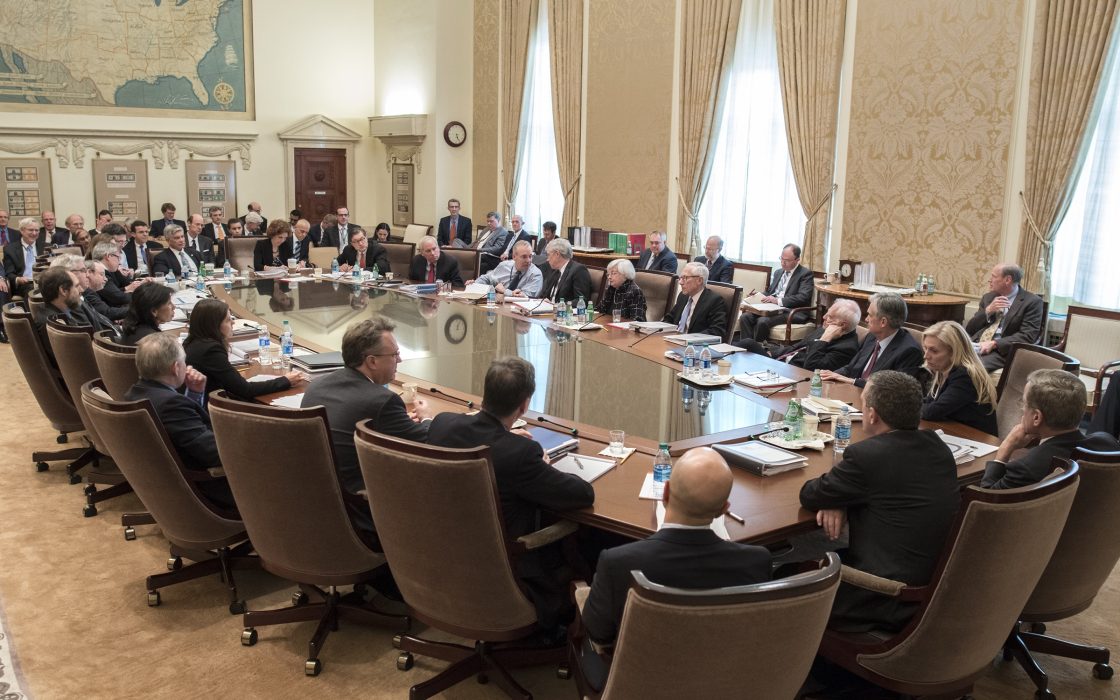 FOMC participants and staff seated around a large conference table in the Federal Reserve Board Room