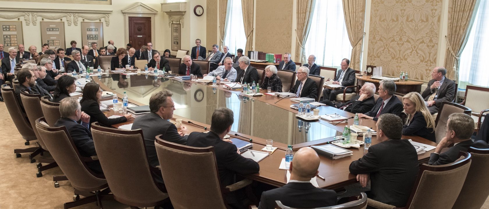 FOMC participants and staff seated around a large conference table in the Federal Reserve Board Room