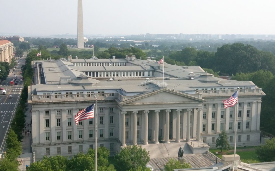 Aerial view of the neoclassical US Treasury Building with American flags and the Washington Monument in the background