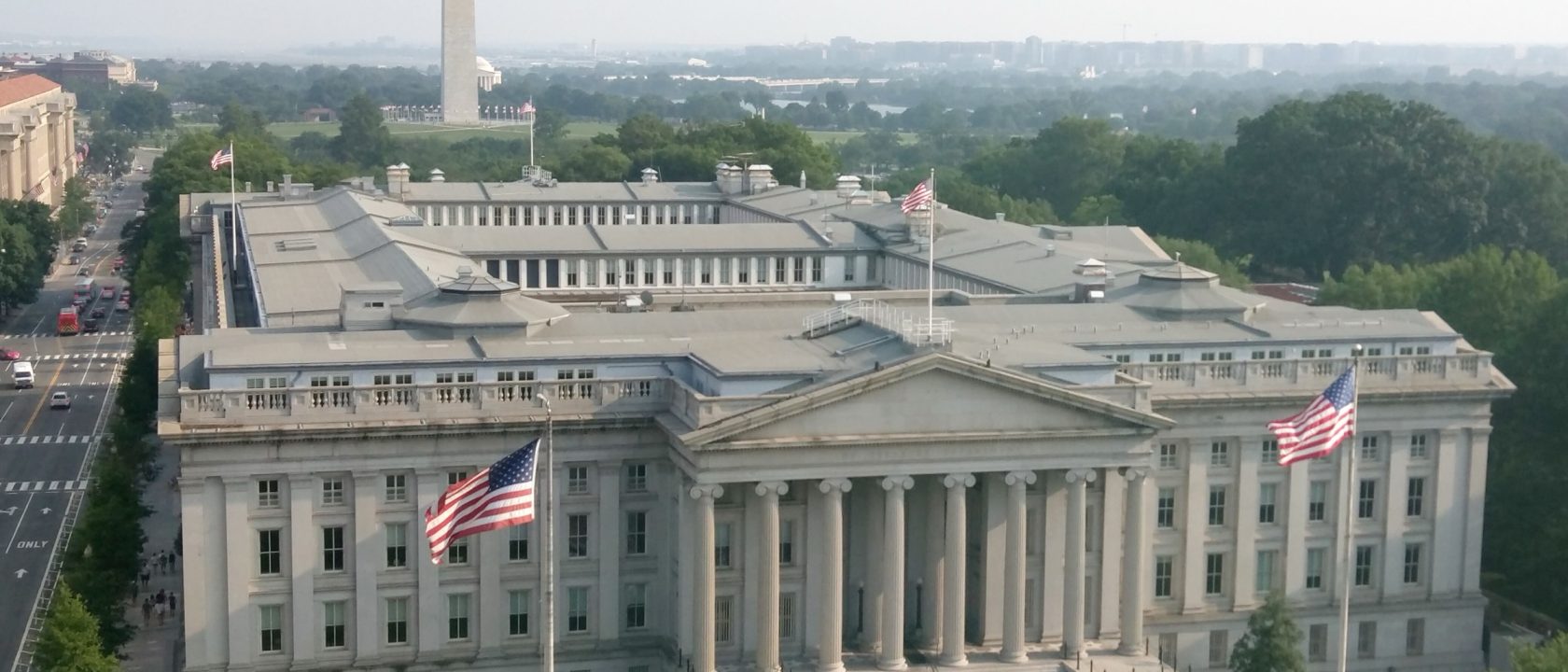 Aerial view of the neoclassical US Treasury Building with American flags and the Washington Monument in the background