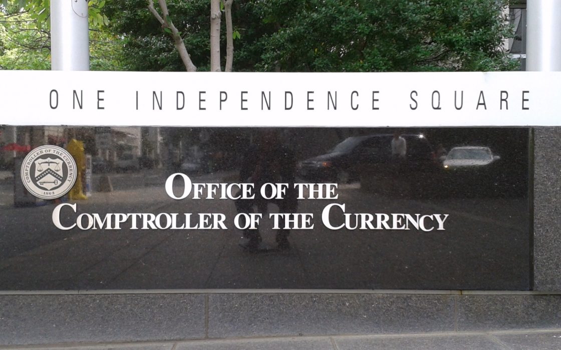 Polished black granite sign reading Office of the Comptroller of the Currency beneath a One Independence Square banner