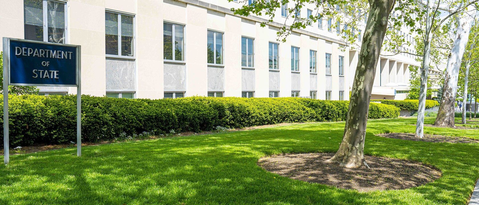 Department of State sign on a green lawn in front of the Harry S. Truman Building