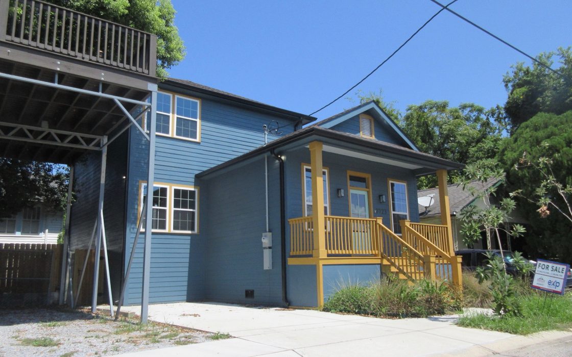 Blue two-story house with a yellow porch and a for-sale sign in the front yard