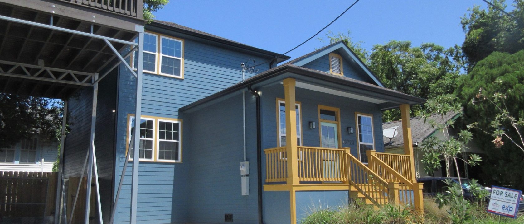 Blue two-story house with a yellow porch and a for-sale sign in the front yard