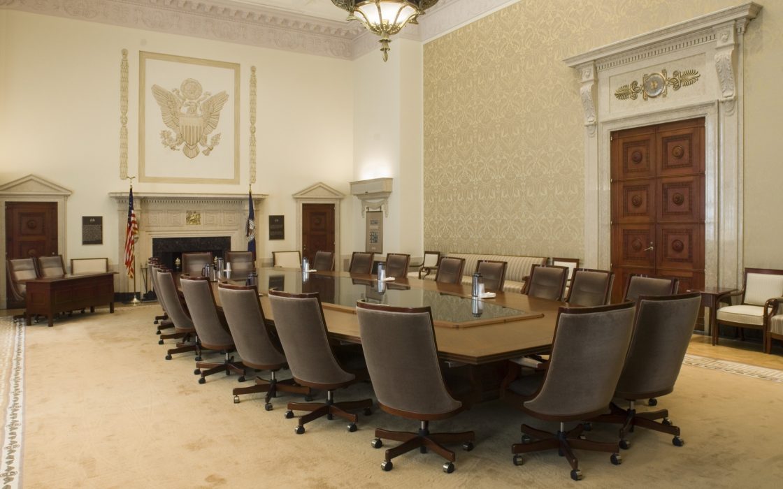 Empty Federal Reserve Board Room with a long conference table, leather chairs and an eagle relief above the fireplace