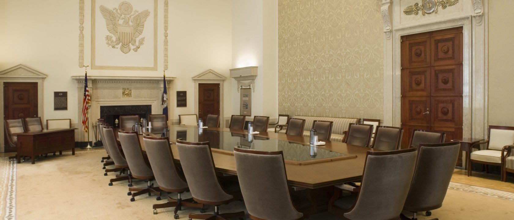 Empty Federal Reserve Board Room with a long conference table, leather chairs and an eagle relief above the fireplace