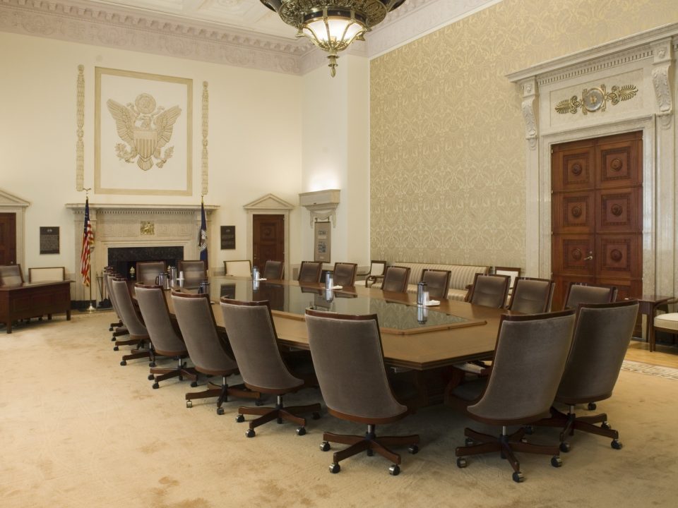 Empty Federal Reserve Board Room with a long conference table, leather chairs and an eagle relief above the fireplace