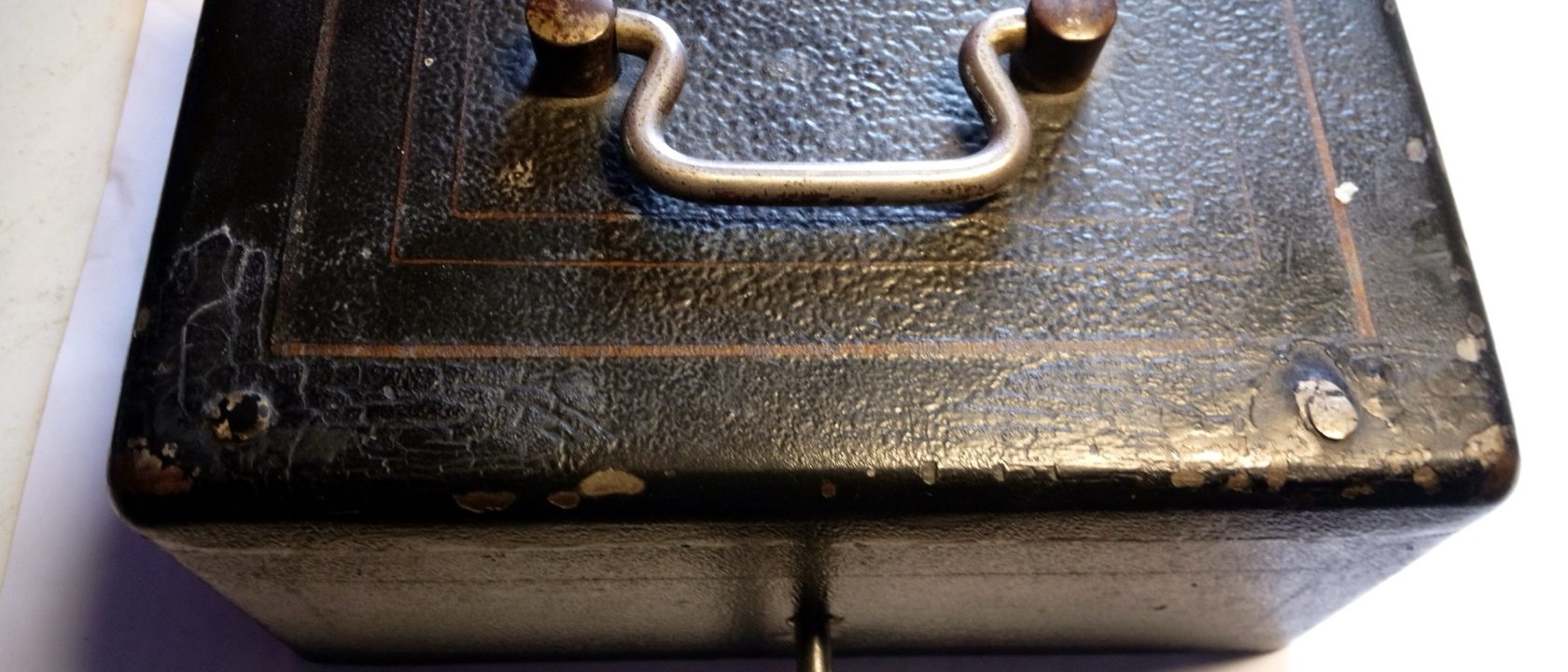 Black embossed metal money box with a brass handle and a key in the lock