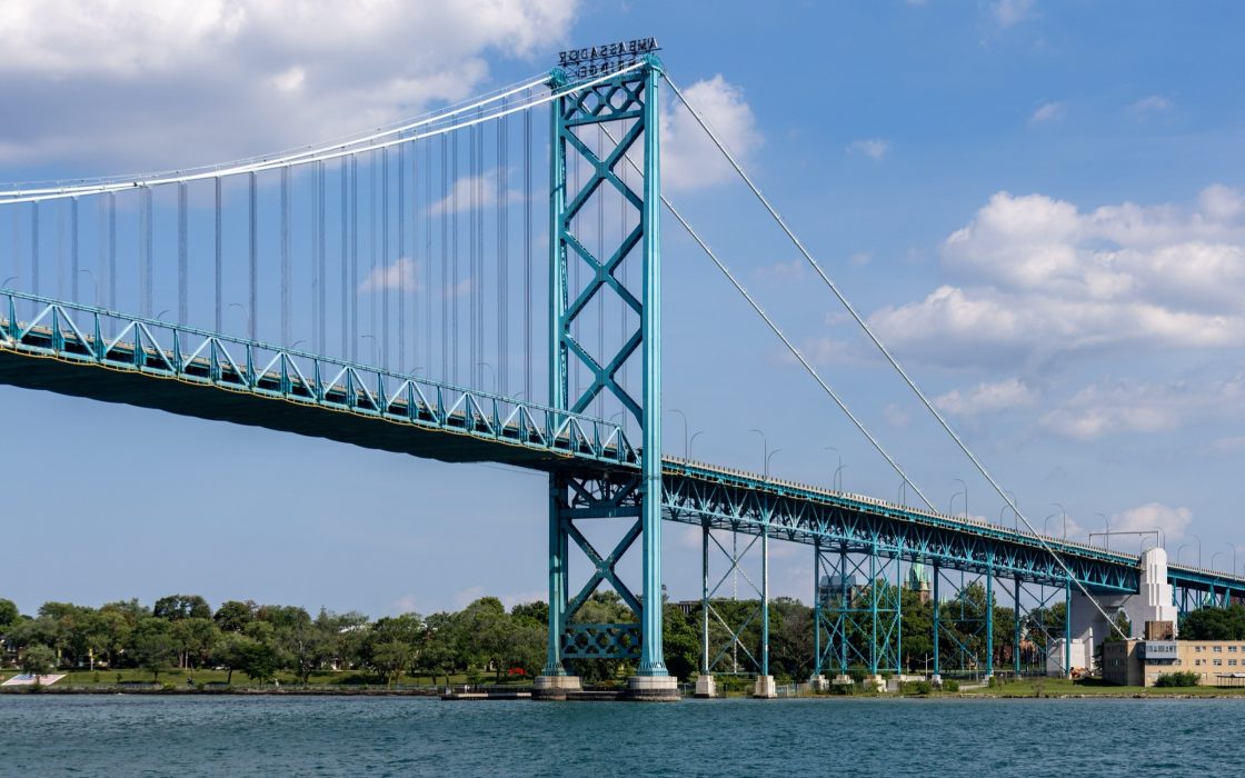 Teal suspension bridge spanning a river under a blue sky with clouds